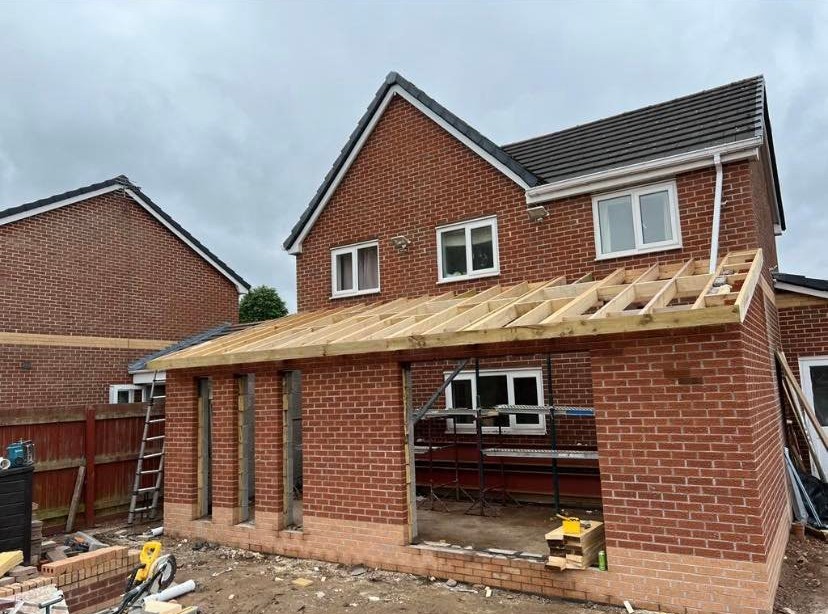 Rear house extension under construction with brick walls and timber roof framing