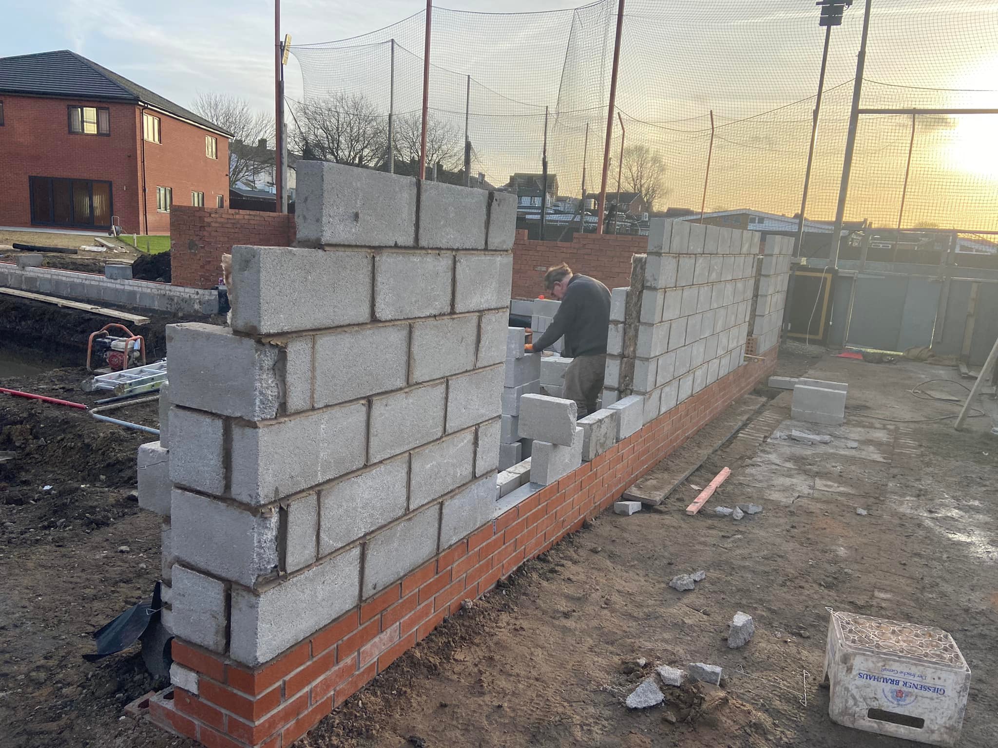 Worker constructing concrete block walls above a brick base