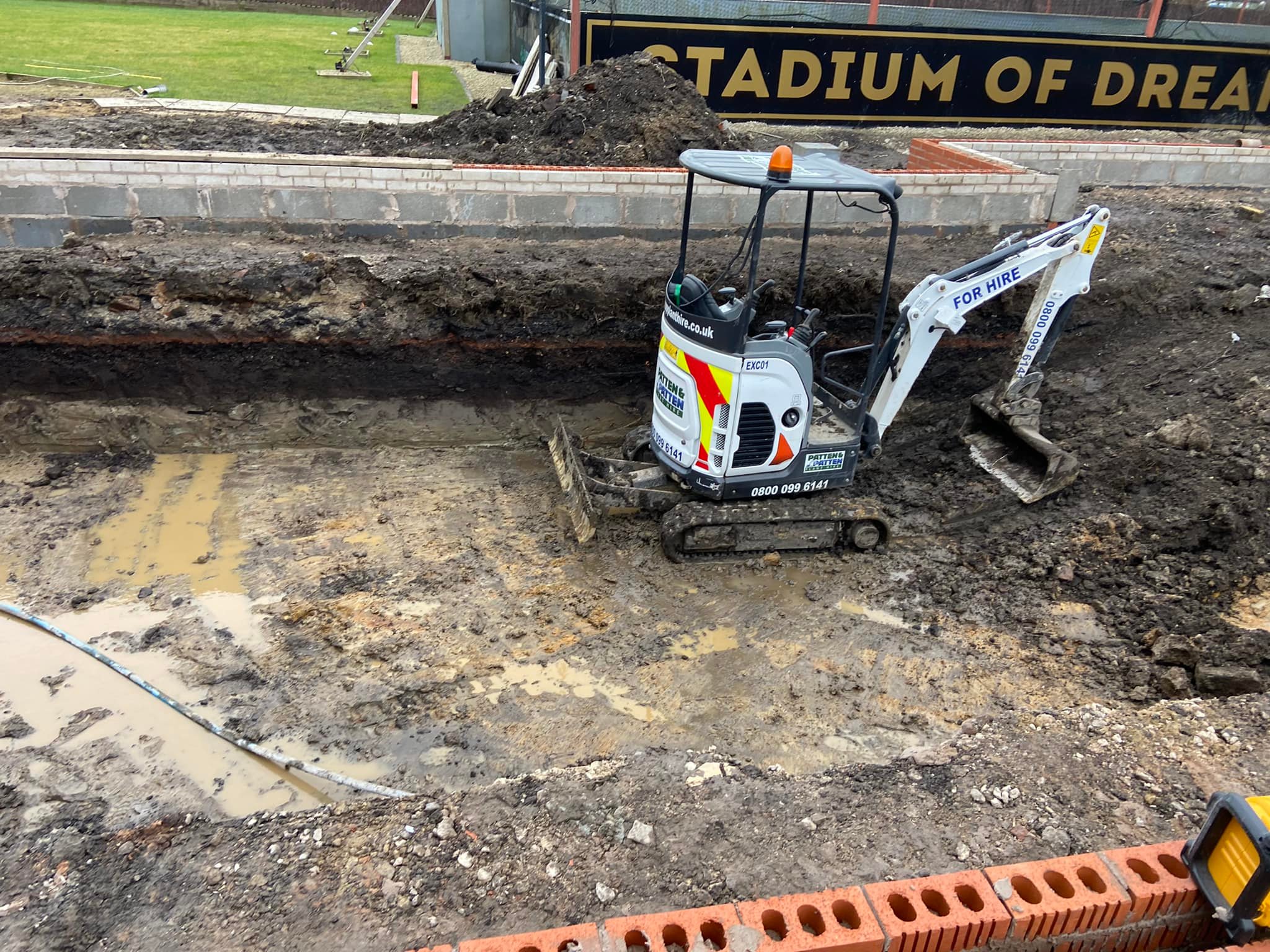 Mini excavator carrying out ground preparation beside garden foundation walls