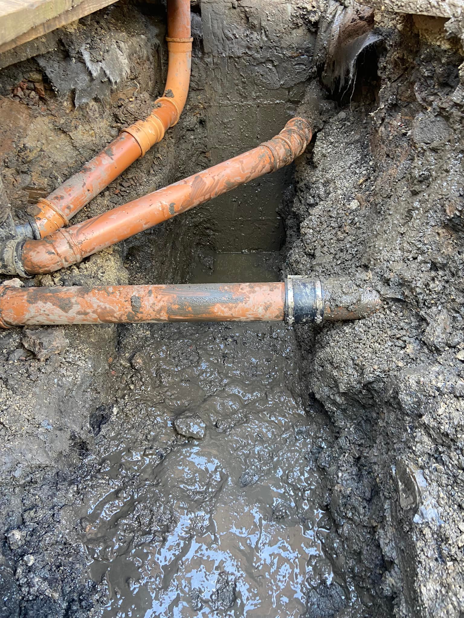 Orange drainage pipes and junctions exposed in an excavated trench